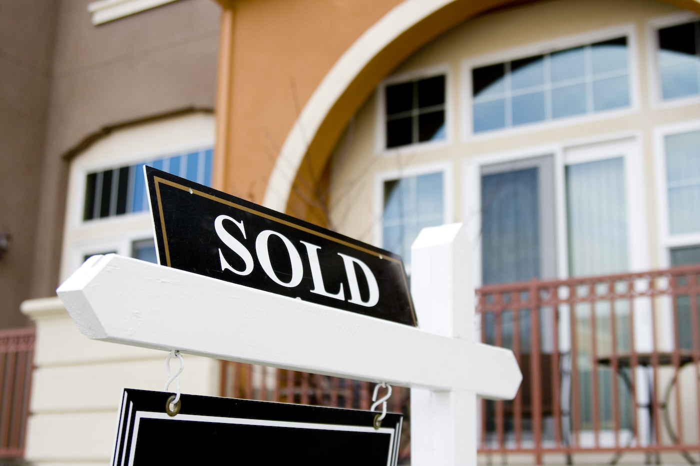 A real estate sign with sold on top of it with a house in the background.