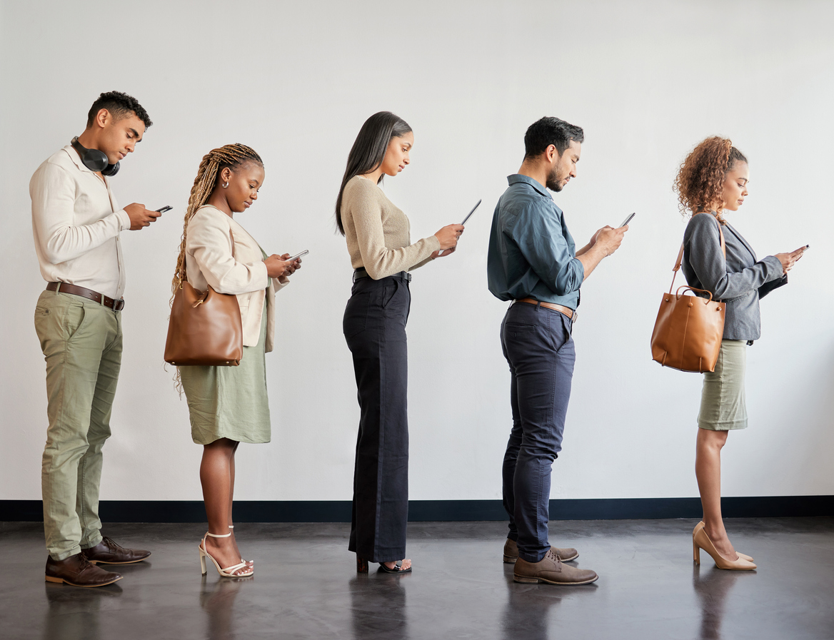 A group of young professionals, symbolizing independent agents, stand in line using smartphones in a modern office, reflecting the importance of agency perpetuation plans and identifying diverse funding sources for future business growth.